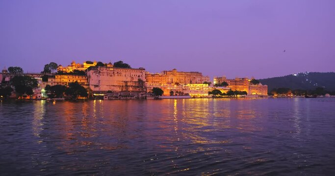Famous luxury Udaipur City Palace on bank Pichola lake illuminated on sunset with water ripples, Rajput architecture of Mewar dynasty rulers. Udaipur, Rajasthan, India, Asia