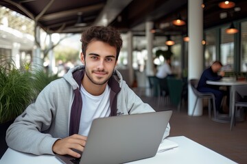 Fototapeta premium Portrait of Cheerful Male Student Learning Online in Coffee Shop, Young European Man Studies with Laptop in Cafe, Doing Homework