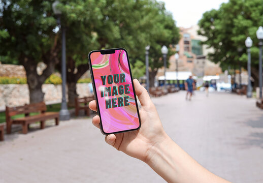 Mockup of person holding mobile phone with customizable screen in city scene