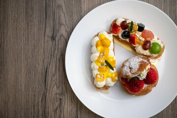 Delicious choux pastry with custard, assorted fruits and icing powder on wooden background.