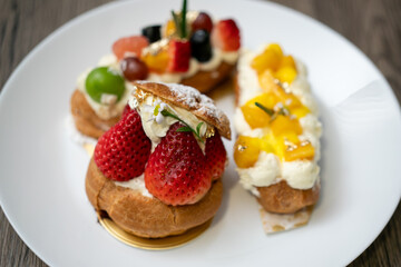 Delicious choux pastry with custard, assorted fruits and icing powder on wooden background.