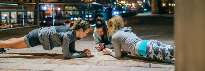 Young women friends sport team doing plank exercise during training together on the empty city at...