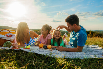 The family is lying on a blanket surrounded by fruit, having a picnic for the last day of summer vacation