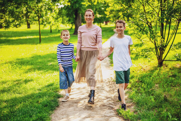 Fototapeta premium Happy mother is walking with her sons in park. They are holding hands and enjoying summer day.