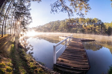 A wooden bridge was built in the middle of the misty lake surface, where the sunlight shined...