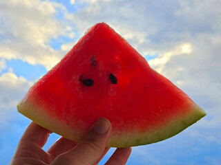Slice of a red, juicy watermelon held in a hand with clear blue sky background. Summer concept.