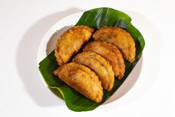 four fried cireng arranged neatly on a wooden plate with a banana leaf base and a plain white backgorund