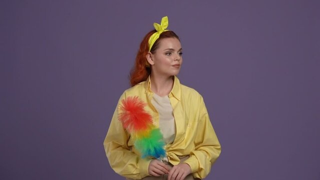 Woman in casual clothing posing at the camera, holding colorful pipidaster brush in hands, smiling face expression. Isolated on purple background.