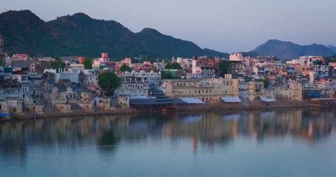 View of famous indian hinduism pilgrimage town sacred holy hindu religious city Pushkar with Brahma temple, aarti ceremony, lake and ghats illuminated at sunset. Rajasthan, India. Horizontal pan