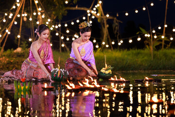 thai woman holding a krathong sitting on a raft by the river, Asian women in traditional Thai costumes bring krathongs to float on Loi Krathong Day, traditions and culture of Thailand,