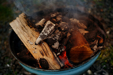 burning fire in compact grill, wood logs engulfed red flames, closeup of metal grill on burning...