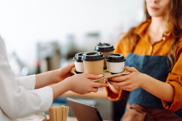 Close-up of a female barista's hands giving out a to-go drink order. The coffee shop owner gives...