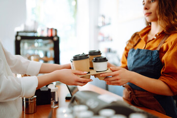 Close-up of a female barista's hands giving out a to-go drink order. The coffee shop owner gives...