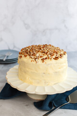 Three tier hummingbird or carrot cake with cream cheese frosting and pecan nuts or walnuts on a white cake stand