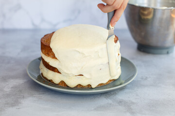 Cream cheese icing being spread on a three tier baked hummingbird cake