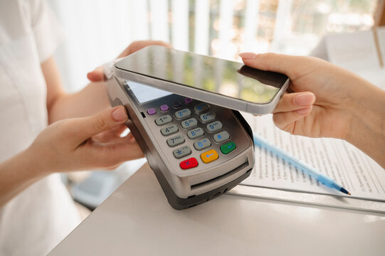 Hand of woman paying through smart phone on credit card reader at clinic