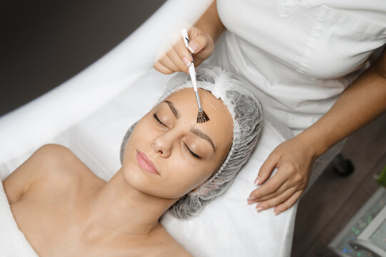 Dermatologist applying chemical peel with brush on woman's face