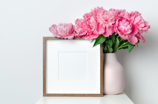 Square picture frame mockup with pink fresh peony flowers in white room interior