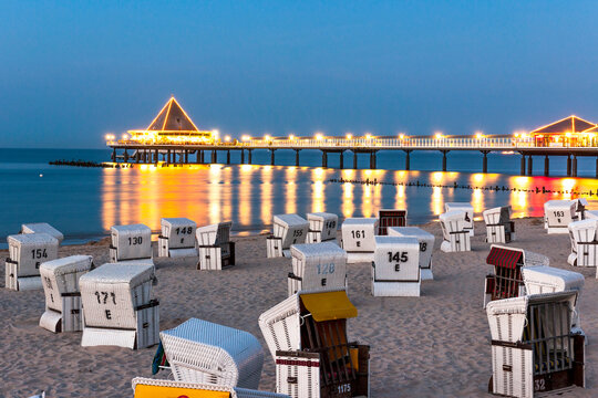 Germany, Mecklenburg-Vorpommern, Ahlbeck, Hooded beach chairs and illuminated pier at dusk