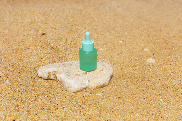 A bottle of face serum stands on a natural stone against the backdrop of a sandy beach