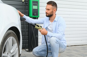 Man Holding Power Charging Cable For Electric Car In Outdoor Car Park. And he s going to connect the car to the charging station in the parking lot near the shopping center.