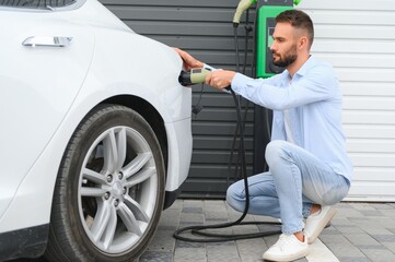 Stylish man inserts plug into the electric car charging socket
