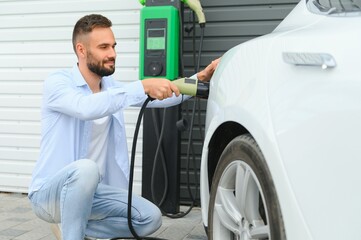 Stylish man inserts plug into the electric car charging socket