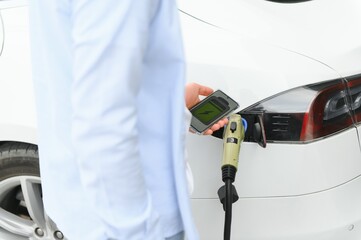 Happy man using smart phone and charging car at vehicle charging station