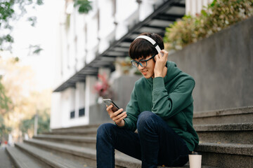 Smiling young man relaxing at home, she is playing music using smartphone tablet, laptop, and wearing white headphones.