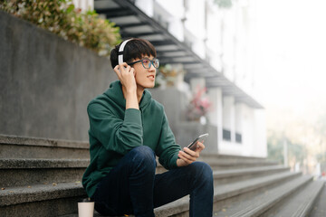 Smiling young man relaxing at home, she is playing music using smartphone tablet, laptop, and wearing white headphones.