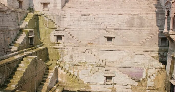 Toorji Ka Jhalra Baoli stepwell and water storage inside it, one of water sources in Jodhpur, Rajasthan, India. Sunny day, water ripples reflect walls of the pool. Camera vertical pan