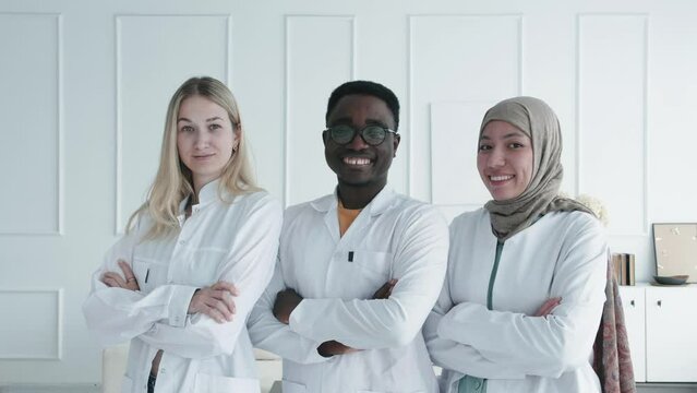 Three professional international interns doctors with crossed arms. Multiethnic international Team of Scientists, doctors and medical workers smiling and feeling confident at clinic hospital 