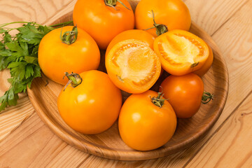 Yellow tomatoes and fresh parsley on wooden dish close-up