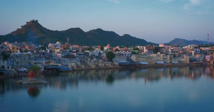 View of famous indian hinduism pilgrimage town sacred holy hindu religious city Pushkar amongst hills with Brahma mandir temple, lake and traditional ghats at sunset. Rajasthan, India. Horizontal pan