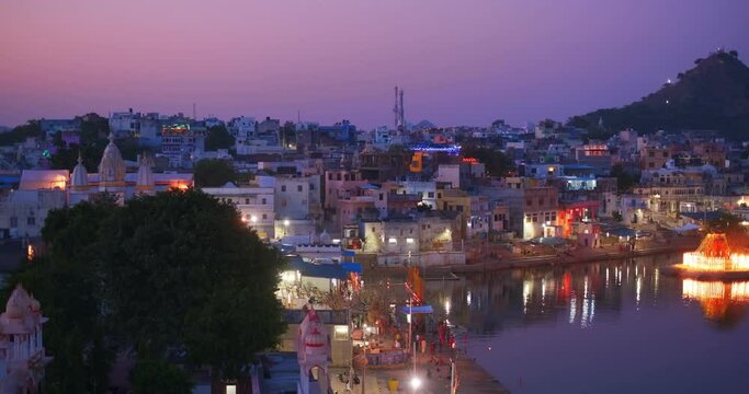View of famous indian hinduism pilgrimage town sacred holy hindu religious city Pushkar with Brahma temple, aarti ceremony, lake and ghats illuminated at sunset. Rajasthan, India. Horizontal pan