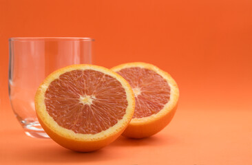 An orange cut in half next a glass with copy space at an orange background