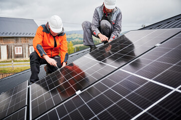 Technicians installing photovoltaic solar panels on roof of house. Men engineers in helmets...