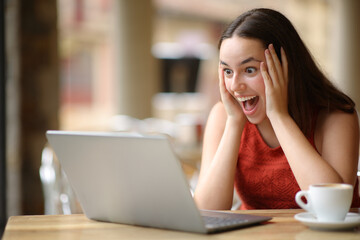Amazed woman finding good news on laptop in a bar