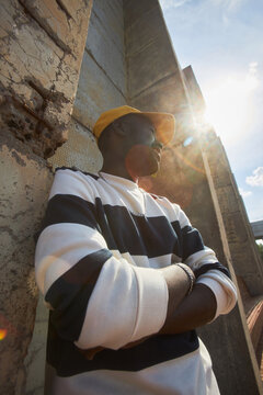 Low angle fashion portrait of trendy black man looking away in sunlight with lens flare