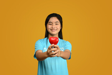 Teenager asian girl wearing volunteer t-shirt isolated on yellow background. Charity, support,...