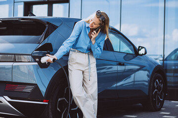 Business woman talking on the phone and standing by her electric car