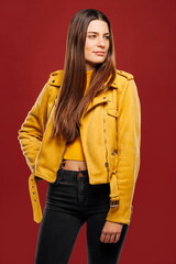 Attractive trendy young female hipster in yellow jacket, looking away isolated over red background at studio.