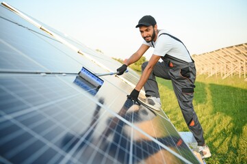 Male arab engineer standing on field with rows of solar panels.
