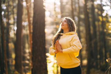 An active woman in sportswear performs yoga exercises in the autumn forest on fallen leaves,...