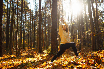 An active woman in sportswear performs yoga exercises in the autumn forest on fallen leaves, catches zen, meditation, relaxation. The concept of relaxation, freedom.