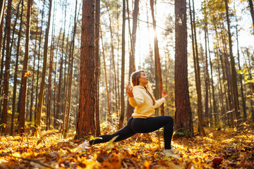 An active woman in sportswear performs yoga exercises in the autumn forest on fallen leaves,...
