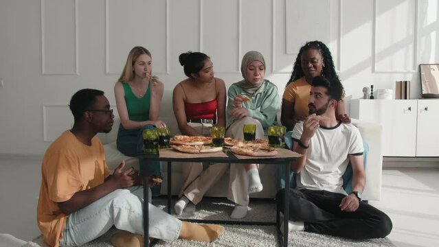 Happy multiracial diverse friends enjoying communicating chatting relaxing eating tasty italian pizza at home. Group of happy men and women eating pizza talking and laughing