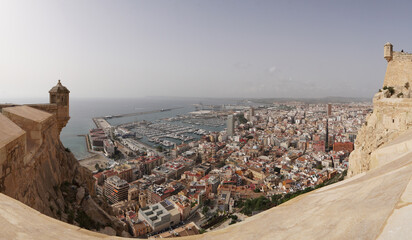 Panorámica de Alicante entre las gritas del castillo de santa bárbara ,  vista aérea de la ciudad. - obrazy, fototapety, plakaty