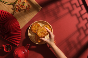 Traditional concept for advertising on Mid-autumn festival. Hand of woman picking a delicious mooncake from bamboo tray. Blank space for display product or design. Copy space
