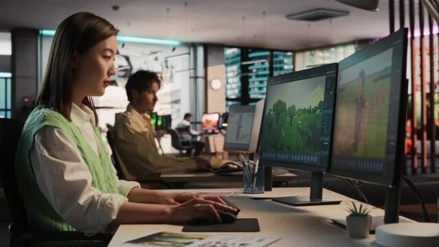 Asian Woman Using Desktop Computer And Designing In 3D modelling Software Unique World And Characters For Survival Video Game In Diverse Office. Female Game Designer Creating Immersive Gameplay.
